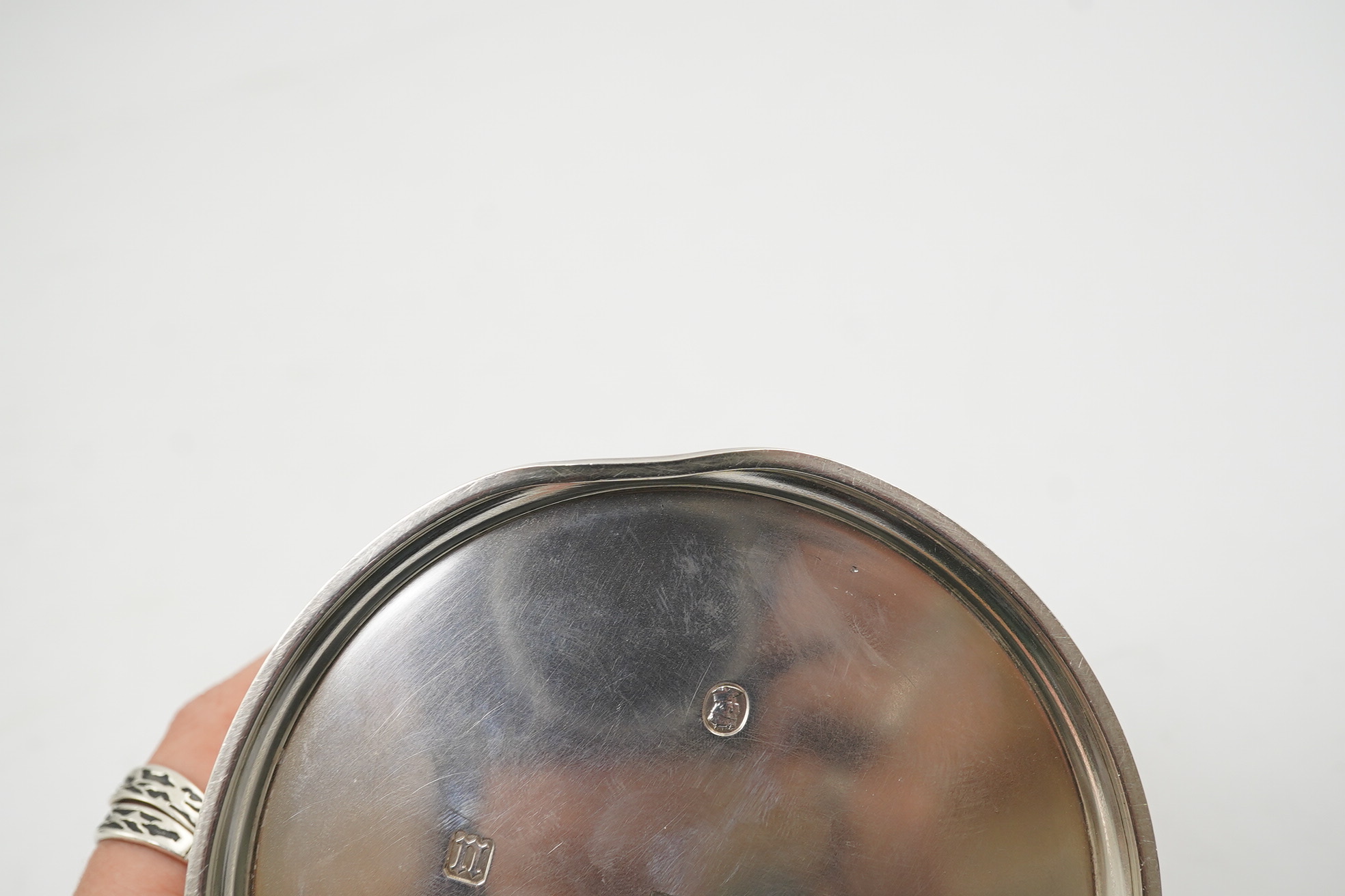 A George V silver circular inkwell, by Sebastian Garrard, commemorating the Silver Jubilee of King George V, the die stamped cover designed by George Kruger Gray featuring the Goldsmiths Company Coat of Arms